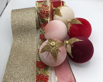 May include: A collection of Christmas ornaments and ribbons. The ornaments are velvet spheres in cream, pink, red, and burgundy, with gold beaded accents. Ribbons include a gold glitter ribbon, and ribbons with poinsettia and gold designs.