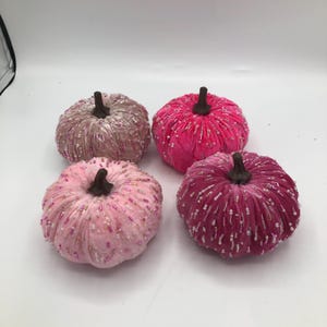 May include: Four decorative velvet pumpkins in shades of pink, fuchsia, and mauve. Each pumpkin has a brown stem and is embellished with beads. These fall-themed decorations are perfect for adding a touch of elegance to any autumn display.