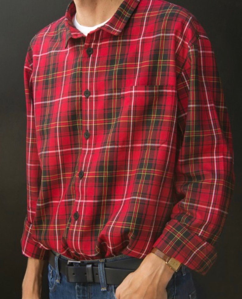 May include: Red plaid button-down shirt with black buttons and a chest pocket. The shirt has a classic plaid pattern in red, black, yellow, and white. The shirt is worn with blue jeans and a black belt.