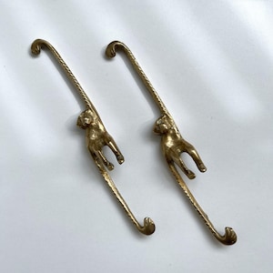 May include: Two gold monkey-shaped hooks. The monkeys are hanging upside down with their tails forming the hook.