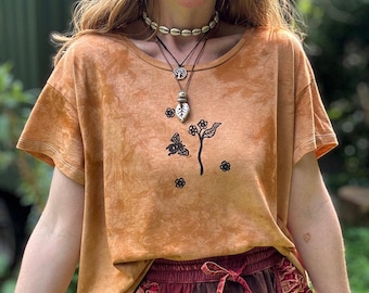 May include: A tie-dye orange t-shirt with a black butterfly and floral design. The shirt has short sleeves and a round neckline. The model is also wearing a shell choker necklace and a pendant necklace.