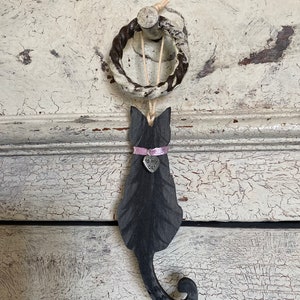 May include: Black wooden cat silhouette hanging from a rope ring with a pink ribbon and a silver charm that says "I love my cat".