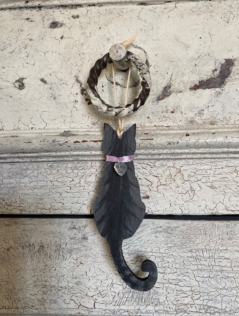 May include: Black wooden cat silhouette hanging from a rope ring with a pink ribbon and a silver charm that says "I love my cat".