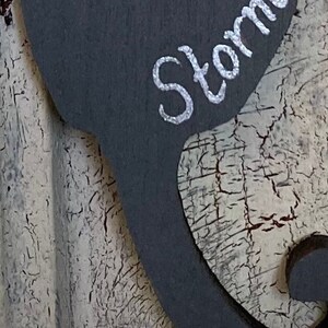 May include: A gray wooden sign with a black silhouette of a mustache and the word "Storm" written in white paint.