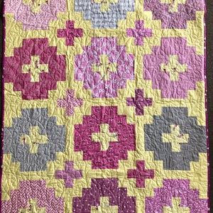 May include: A quilt with a patchwork design featuring yellow, pink, and gray squares. The quilt is made up of different patterns, including floral, polka dot, and checkered.
