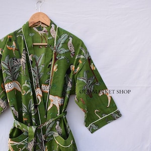 May include: Green cotton robe with a white trim and a jungle print featuring zebras, leopards, toucans, and palm trees. The robe has a tie belt and two pockets.