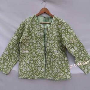 May include: A green quilted jacket with a white floral pattern. The jacket has a zipper closure and a green and white striped lining.