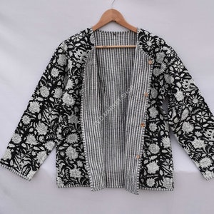 May include: Black and white quilted jacket with a floral print and striped lining. The jacket has a button closure and long sleeves.