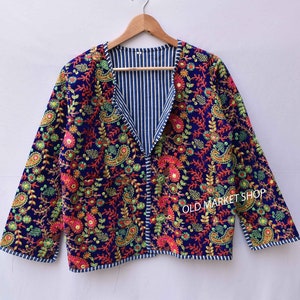 May include: A blue embroidered jacket with a floral pattern and a striped lining. The jacket has a V-neck and long sleeves. The text "OLD MARKET SHOP" is visible on the right sleeve.