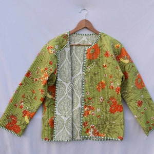Può includere: Una giacca trapuntata verde con una stampa floreale in tonalità arancio e giallo. La giacca ha una fodera bianca con un motivo paisley e un bordo verde.
