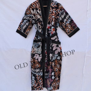 May include: A black kimono-style robe with a floral pattern in shades of brown, white, and purple. The robe has a black belt and trim, and is hanging on a wooden hanger. The text "OLD SHOP" is visible.