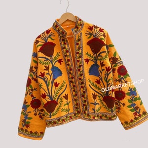 Puede incluir: Una chaqueta amarilla bordada con un patr&oacute;n floral en tonos rojos, azules y verdes. La chaqueta tiene un cuello mandar&iacute;n y un cierre frontal.