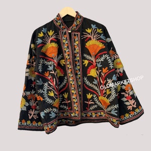 Puede incluir: Una chaqueta negra bordada con motivos florales coloridos. La chaqueta tiene un cuello mandar&iacute;n y un cierre de bot&oacute;n. El bordado es intrincado y detallado, y los colores son vibrantes y llamativos.