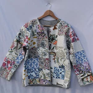 Pode incluir: Uma jaqueta acolchoada branca com um design de patchwork que apresenta padrões florais e geométricos em tons de rosa, azul, verde e laranja. A jaqueta tem um fecho de correr e uma gola listrada.