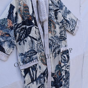 May include: White, long, open-front robe with a botanical print in shades of blue, teal, and peach. The robe features a matching belt and is accented with white stitching. The design includes leaves and bird-like figures.