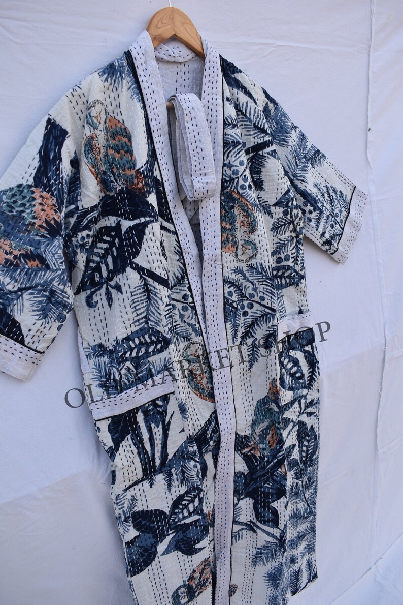 May include: White, long, open-front robe with a botanical print in shades of blue, teal, and peach. The robe features a matching belt and is accented with white stitching. The design includes leaves and bird-like figures.