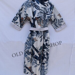 May include: White robe with a blue and tan botanical print. The robe features a matching belt and short sleeves. The fabric is patterned with leaves, birds, and other natural elements. The robe is hanging on a wooden hanger.