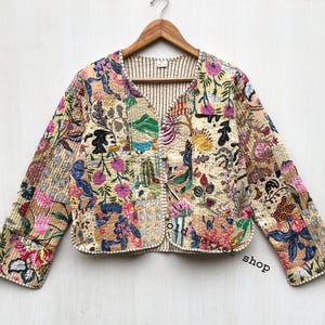May include: A cream-colored quilted jacket with a floral patchwork design. The jacket has a V-neck and long sleeves. The fabric is a mix of beige, pink, green, and blue.