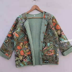 Pode incluir: Uma jaqueta acolchoada verde e cinza com estampa floral. A jaqueta tem um forro listrado e um fecho de botão.