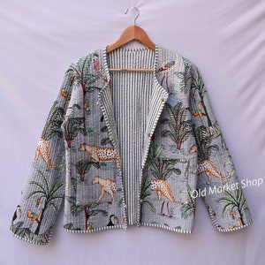 Puede incluir: Una chaqueta acolchada a rayas grises y blancas con un estampado de jungla con tucanes, leopardos y palmeras. La chaqueta tiene una cremallera y un cuello. El texto "Old Market Shop" es visible en el lado derecho de la chaqueta.