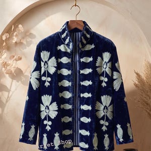 May include: A deep blue velvet jacket featuring a high collar and long sleeves, adorned with light green embroidered floral and abstract patterns. The front closure consists of multiple fabric-covered toggle buttons, and the interior lining displays a vertical blue and white striped design.