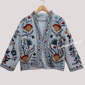 Puede incluir: Una chaqueta azul claro bordada con motivos florales en rojo, azul, verde y marr&oacute;n. La chaqueta tiene un cuello mandar&iacute;n y un cierre frontal.