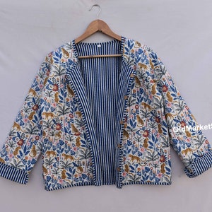 以下が含まれることがあります： 片面がストライプ柄、もう片面が白地に虎と植物の繰り返し模様が描かれた青と白のリバーシブルジャケット。ジャケットはボタン留め、長袖です。