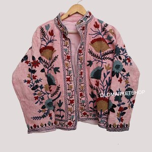 Puede incluir: Una chaqueta rosa bordada con motivos florales en tonos azules, rojos y marrones. La chaqueta tiene un cuello mandar&iacute;n y una cremallera frontal. El texto "OLDMARKETSHOP" es visible en la esquina inferior derecha de la chaqueta.