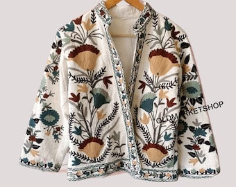 May include: A white linen jacket with a floral embroidery design in shades of brown, green, and beige. The jacket has a mandarin collar and a front button closure. The text "OLDMARKETSHOP" is visible in the bottom right corner of the image.