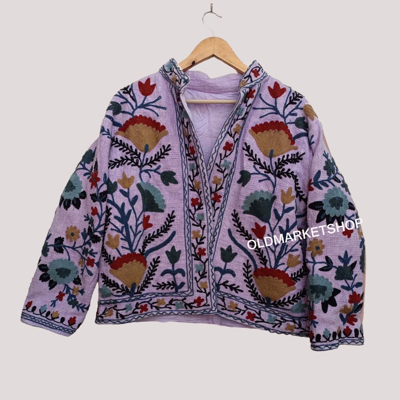 Puede incluir: Una chaqueta de color lavanda con un dise&ntilde;o de bordado floral. El bordado presenta una variedad de colores, incluyendo rojo, verde, azul y marr&oacute;n. La chaqueta tiene un cuello mandar&iacute;n y un cierre de bot&oacute;n.