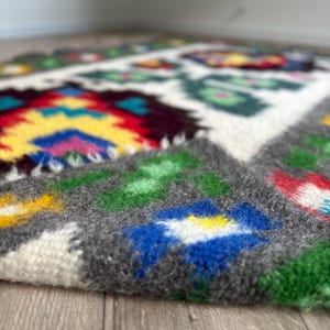 Pu&ograve; includere: Un tappeto tessuto a mano con un motivo geometrico colorato. Il tappeto &egrave; in lana e ha una texture morbida e soffice. I colori del motivo includono rosso, giallo, blu, verde e bianco.