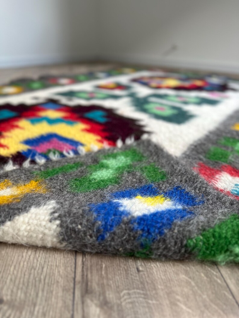 Pu&ograve; includere: Un tappeto tessuto a mano con un motivo geometrico colorato. Il tappeto &egrave; in lana e ha una texture morbida e soffice. I colori del motivo includono rosso, giallo, blu, verde e bianco.