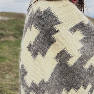 May include: A white and gray woven blanket with a geometric pattern. The blanket is draped over a person's shoulders.