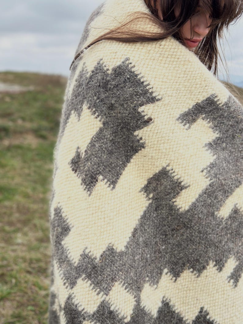 May include: A white and gray woven blanket with a geometric pattern. The blanket is draped over a person's shoulders.
