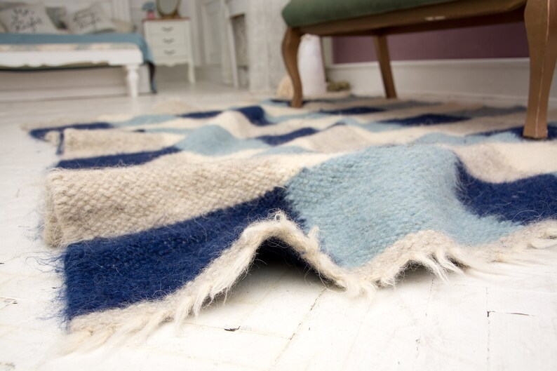 May include: A blue, white and beige striped rug with a fluffy texture. The rug is folded and has a frayed edge.
