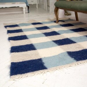 May include: A blue and white checked rug with a fringed edge. The rug is made of wool and has a soft, fluffy texture.