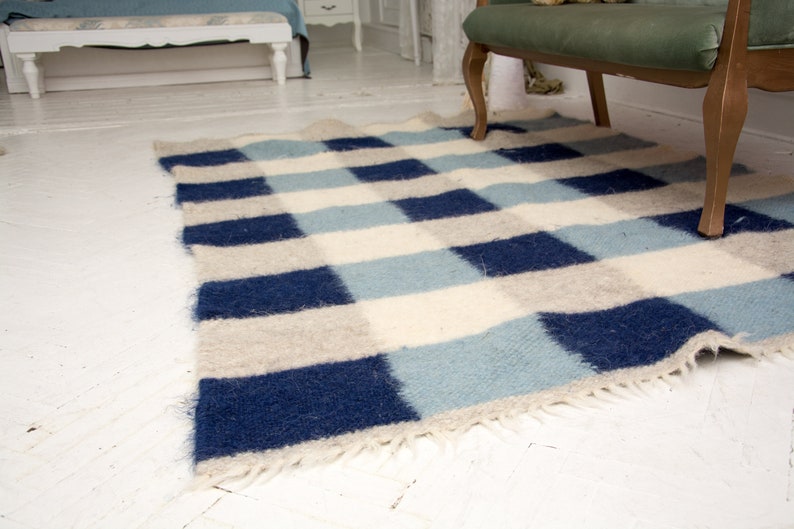 May include: A blue and white checked rug with a fringed edge. The rug is made of wool and has a soft, fluffy texture.
