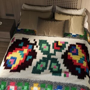 Pu&ograve; includere: Un copriletto bianco con un motivo geometrico colorato che presenta un design ripetitivo di fiori stilizzati. Il copriletto &egrave; su un letto con cuscini in tonalit&agrave; di marrone e beige.
