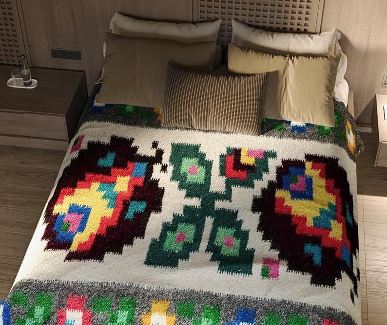 Pu&ograve; includere: Un copriletto bianco con un motivo geometrico colorato che presenta un design ripetitivo di fiori stilizzati. Il copriletto &egrave; su un letto con cuscini in tonalit&agrave; di marrone e beige.
