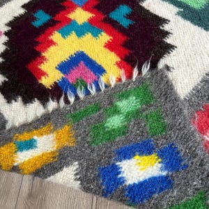 Pu&ograve; includere: Un tappeto colorato tessuto a mano con un motivo geometrico in tonalit&agrave; di rosso, giallo, blu, verde e bianco. Il tappeto ha una texture soffice ed &egrave; fatto di lana.
