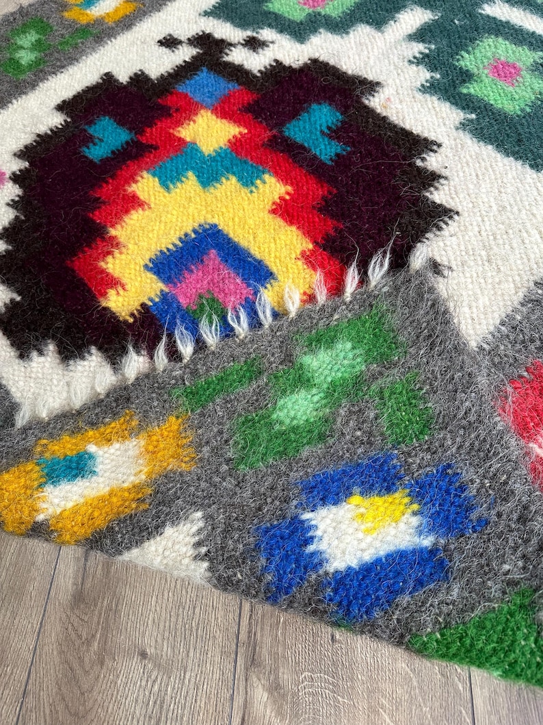 Pu&ograve; includere: Un tappeto colorato tessuto a mano con un motivo geometrico in tonalit&agrave; di rosso, giallo, blu, verde e bianco. Il tappeto ha una texture soffice ed &egrave; fatto di lana.