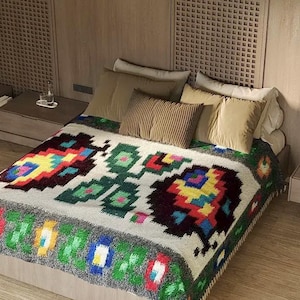 Pu&ograve; includere: Un letto bianco con una coperta a motivi colorati. La coperta ha un design geometrico con colori rosso, giallo, verde e blu. Il letto &egrave; contro una parete di legno con una testata a doghe.