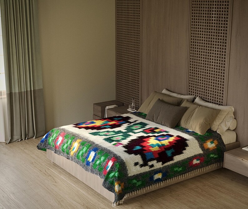 Pu&ograve; includere: Un letto bianco con una coperta colorata a motivi. Il letto &egrave; contro un muro con una testata in pannelli di legno. La coperta ha un design geometrico con colori rosso, verde, blu e giallo.