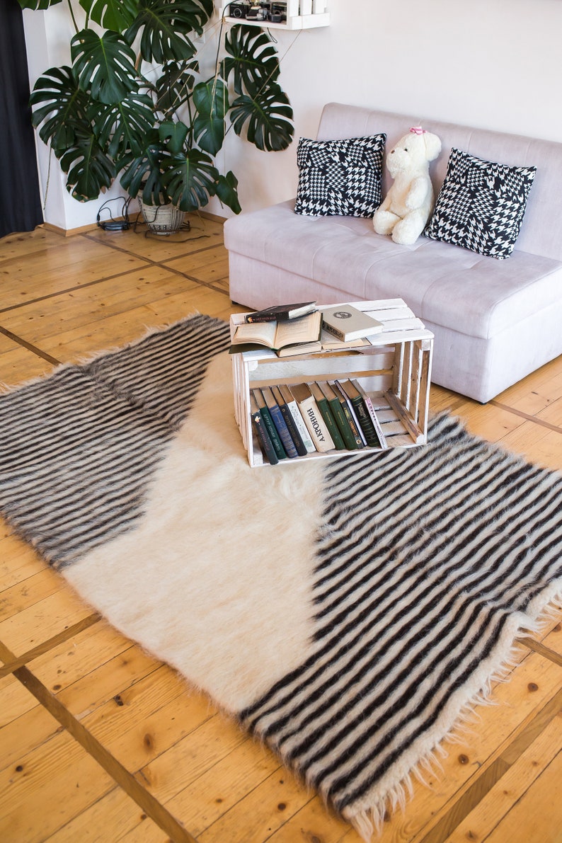 K&ouml;nnte beinhalten: Ein wei&szlig;-schwarz gestreifter Teppich mit flauschiger Textur. Der Teppich liegt auf einem Holzboden vor einem wei&szlig;en Sofa mit schwarz-wei&szlig;en gemusterten Kissen und einem Teddyb&auml;r.