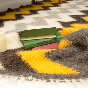 May include: A stack of three books with green, brown, and red covers, resting on a fuzzy, brown and yellow blanket with a zig-zag pattern.
