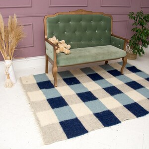 May include: A small green velvet sofa with a wooden frame and a checkered rug in shades of blue, white, and beige.
