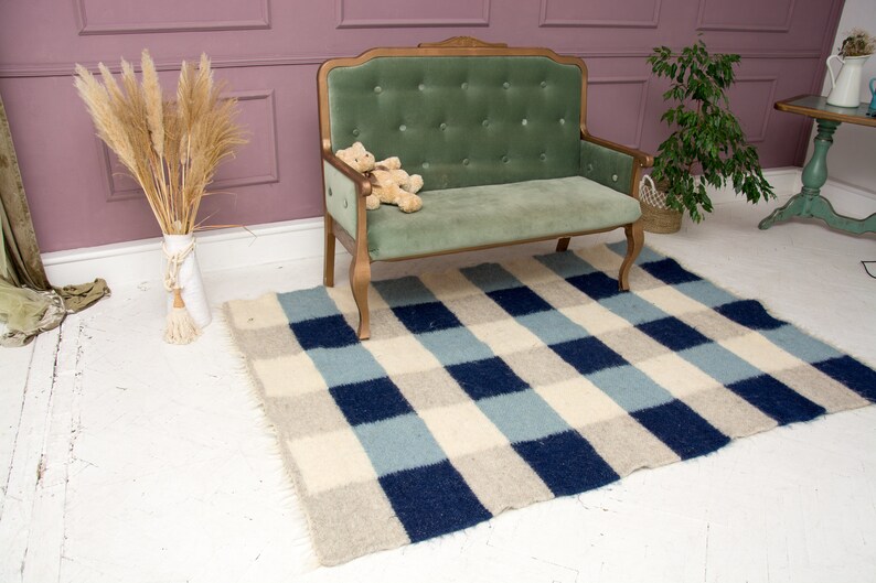 May include: A small green velvet sofa with a wooden frame and a checkered rug in shades of blue, white, and beige.