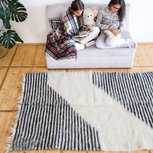 K&ouml;nnte beinhalten: Zwei Personen sitzen auf einem Sofa und lesen B&uuml;cher. Sie sind mit einer karierten Decke bedeckt. Ein wei&szlig;-schwarz gestreifter Teppich liegt auf dem Boden vor dem Sofa.