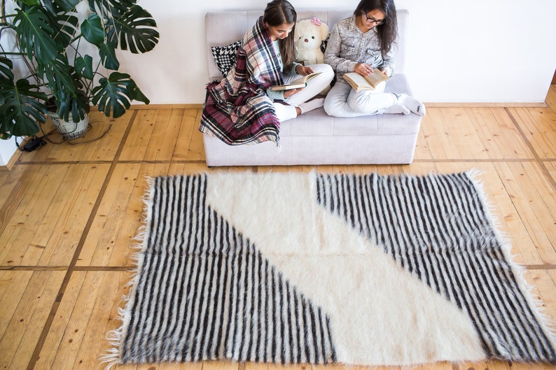 K&ouml;nnte beinhalten: Zwei Personen sitzen auf einem Sofa und lesen B&uuml;cher. Sie sind mit einer karierten Decke bedeckt. Ein wei&szlig;-schwarz gestreifter Teppich liegt auf dem Boden vor dem Sofa.