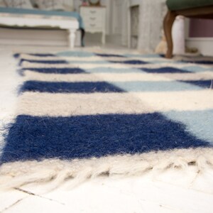 May include: A blue, white and light blue chequered rug with a fluffy texture. The rug has a fringe border.